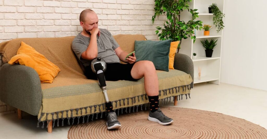 Young man with artificial leg sitting on the couch looking at his mobile | Arnold Dallas McPherson Injury Lawyers