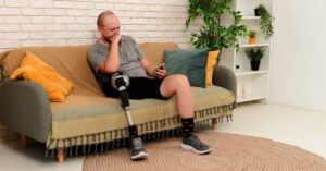 Young man with artificial leg sitting on the couch looking at his mobile | Arnold Dallas McPherson Injury Lawyers